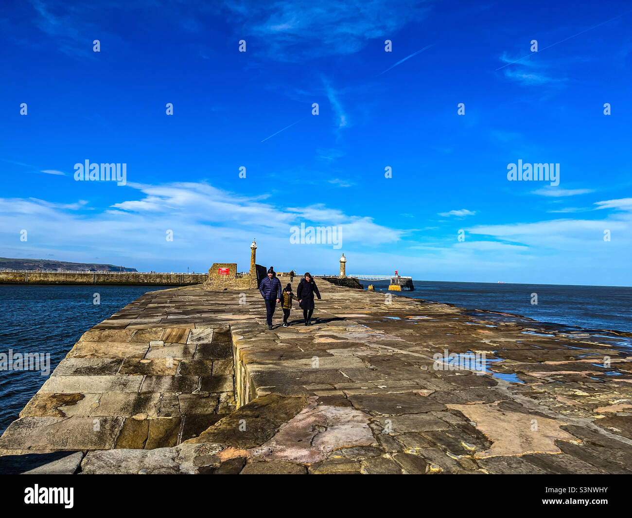 Una giovane famiglia che cammina sul molo di Whitby Foto Stock