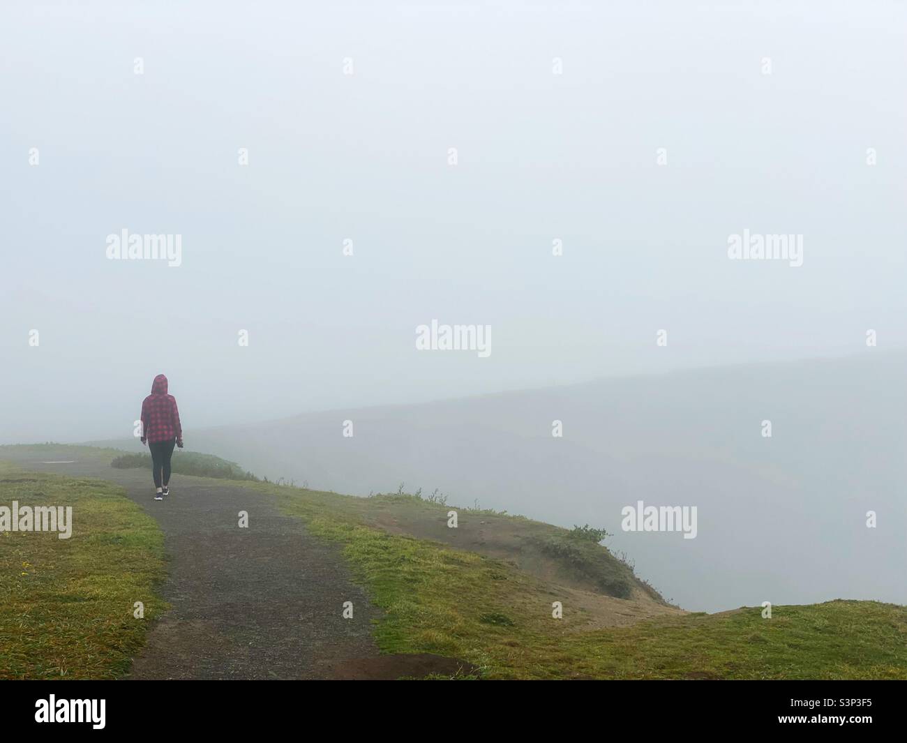 Una persona che cammina su una scogliera di nebbia, vista da dietro. Foto Stock