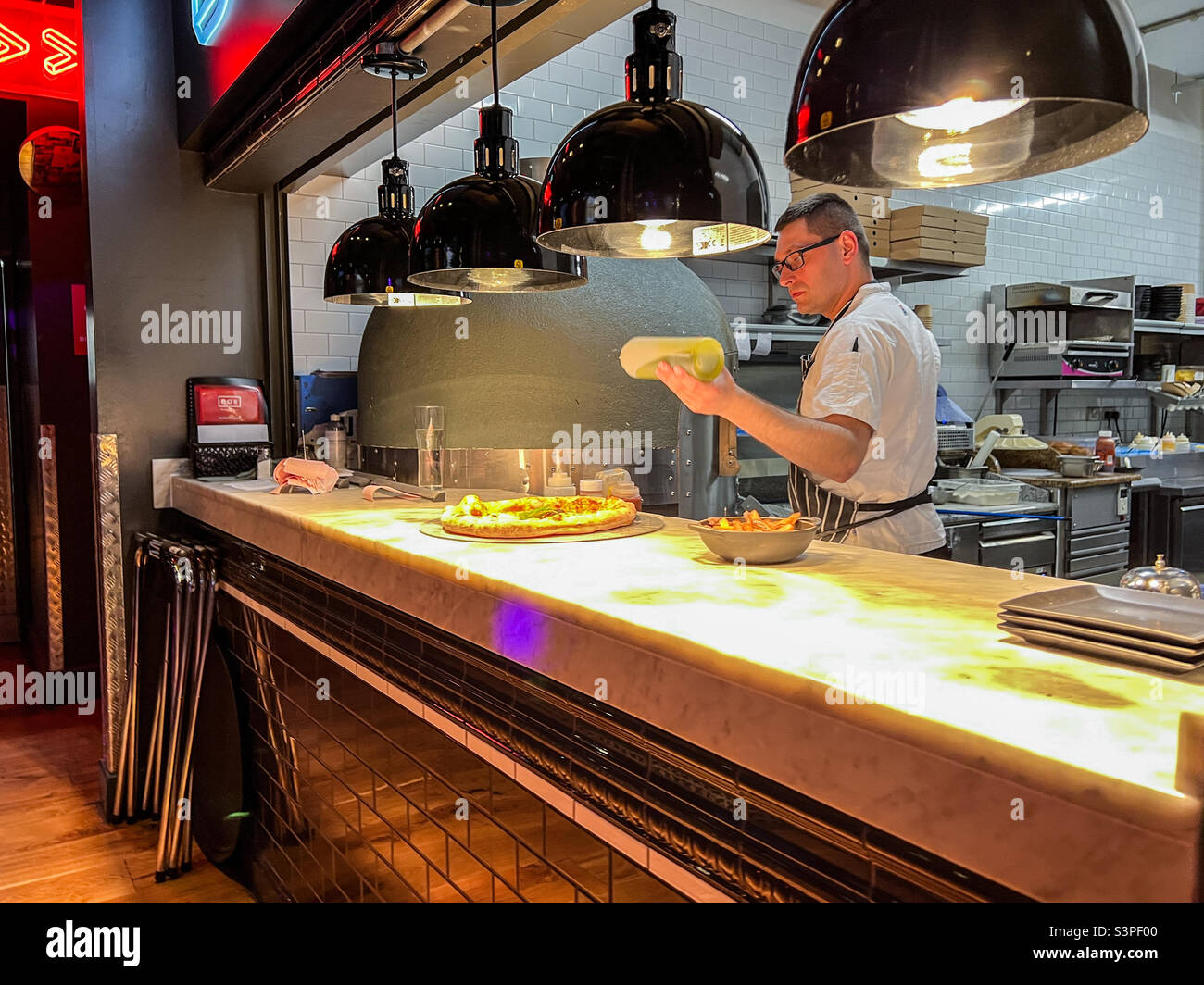 Chef che mette i tocchi di rifinitura su una pizza in un bar ristorante Foto Stock