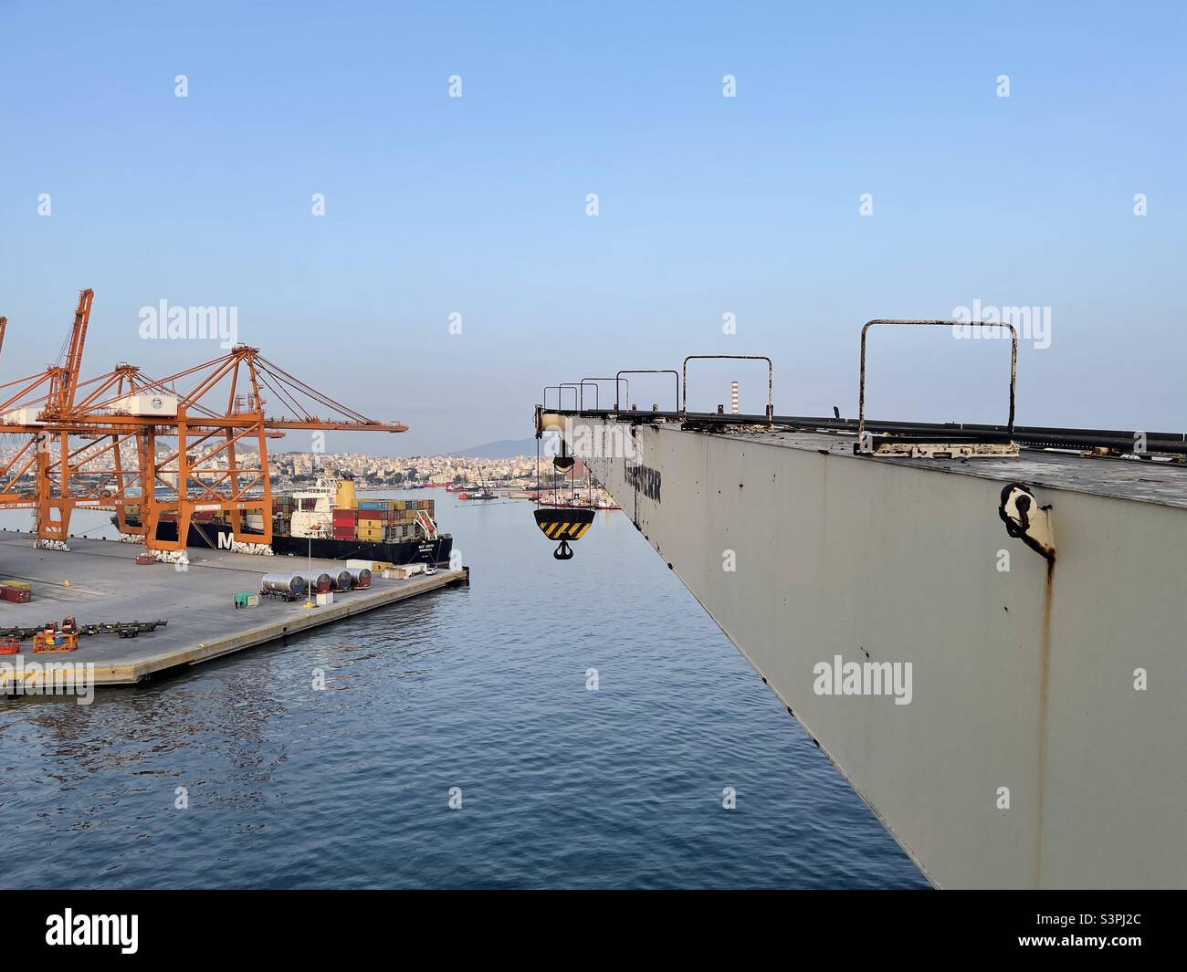 Fiocco con un gancio della gru da carico sulla nave container ormeggiata nel terminal mercantile nel porto di Pireo, Grecia. Sullo sfondo vi sono altri moli con gru a portale e per imbarcazioni durante il funzionamento del carico. Foto Stock