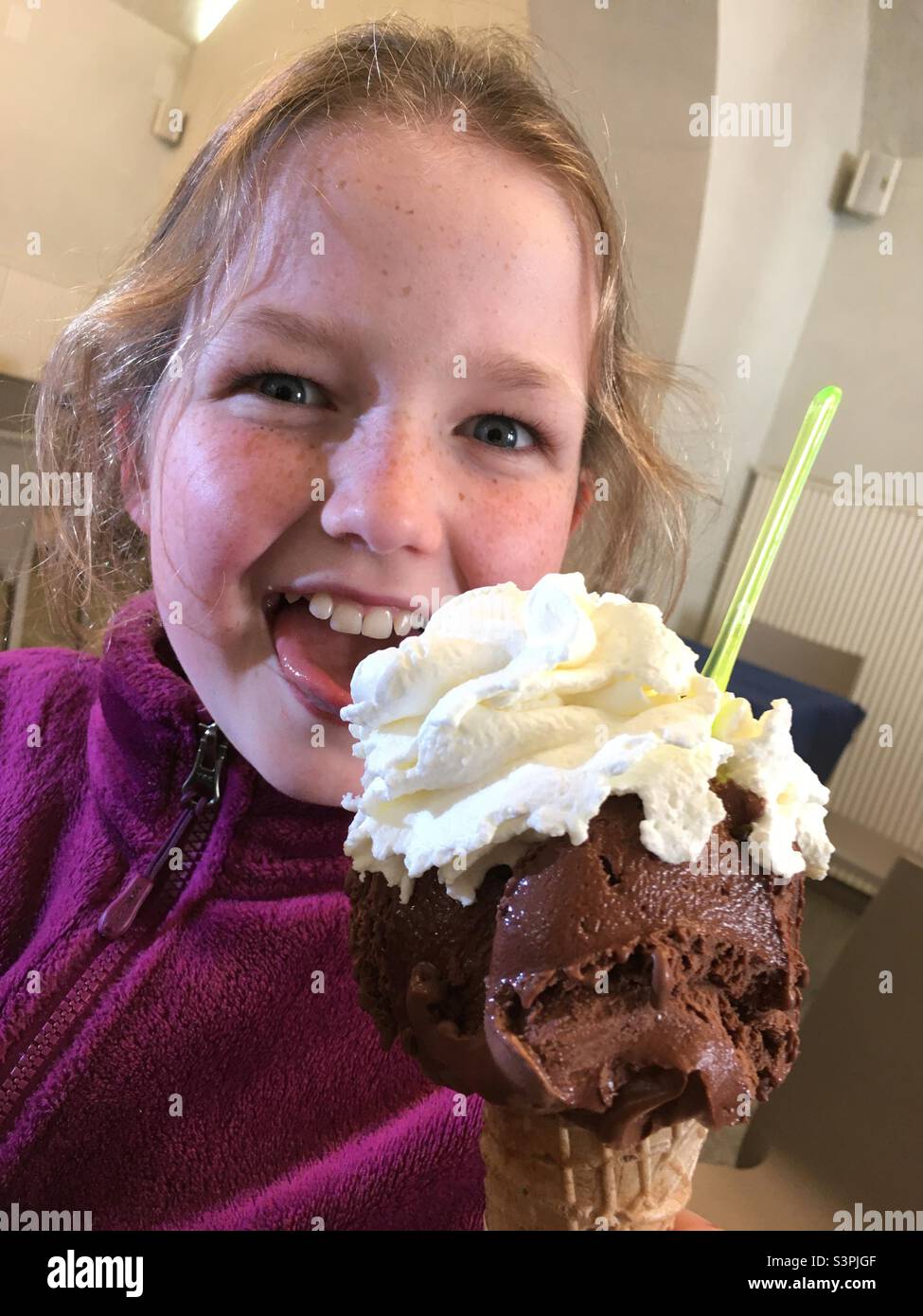 Ragazza di 10 anni che mangia un grande gelato al cioccolato italiano con panna in più, mangiando con ovvia delizia. Foto Stock