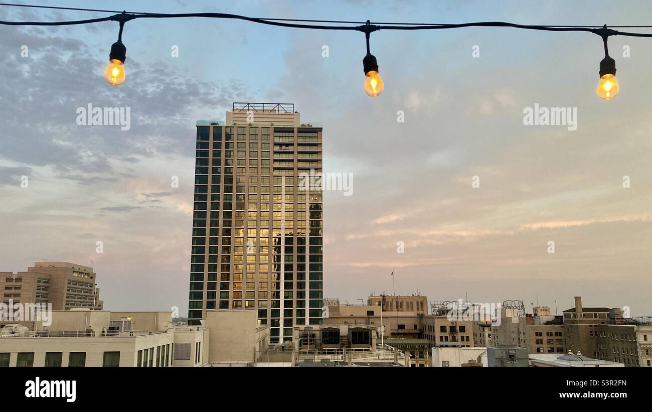 LOS ANGELES, CA, GIUGNO 2021: Nuovo edificio di appartamenti a più piani nel centro città con le nuvole al tramonto e la luce che si riflette sulle finestre. Serie di lampadine in primo piano, parte superiore dell'immagine - Immagine stock catturata con smartphone