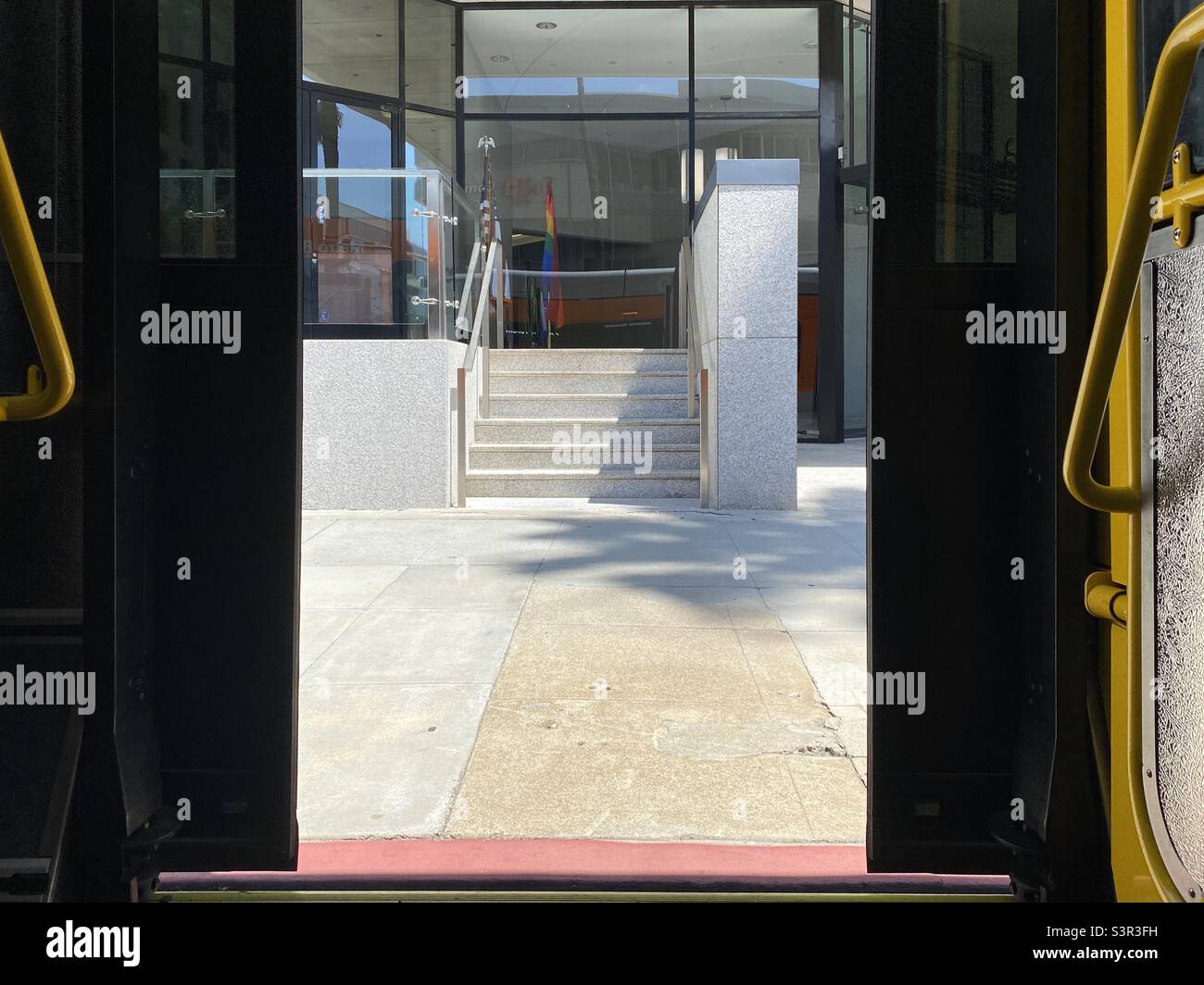 LOS ANGELES, CA, GIUGNO 2021: Vista attraverso le porte dell'autobus alla fermata, guardando le scale che conducono agli uffici con gli Stati Uniti e bandiera arcobaleno - Immagine stock catturata con smartphone