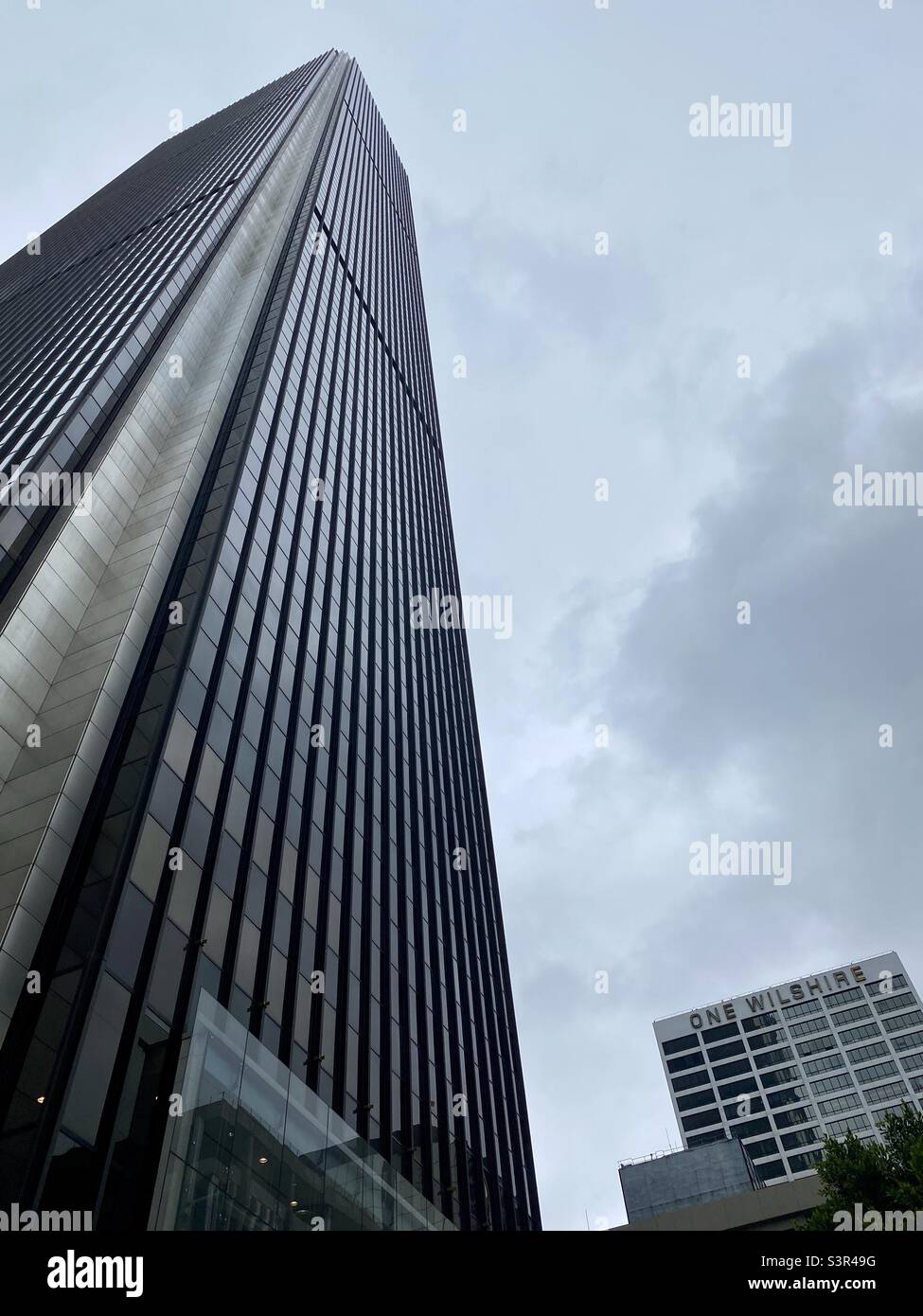 LOS ANGELES, CA, 2021 GIUGNO: IL grattacielo AON Tower raggiunge il cielo nuvoloso con un edificio Wilshire accanto ad esso, Downtown - Immagine stock catturata con smartphone
