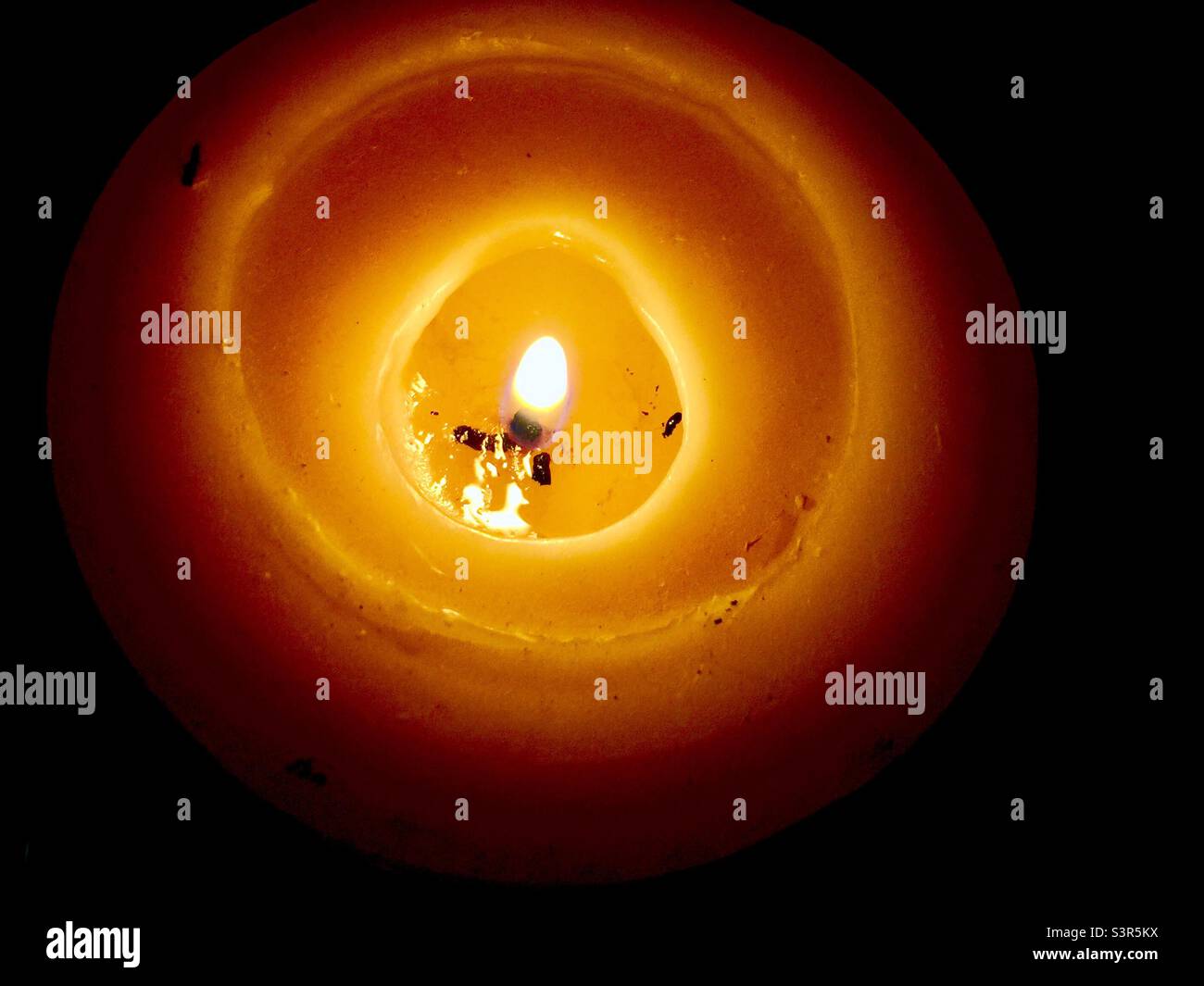 Candela solitaria. Poca fiamma in una piccola pozza di cera fusa. Leggere gentilmente il cavo. Bruciare il bambino. Una candela brucia, diffonde la luce, illumina il calore e le buone vibrazioni. Foto Stock