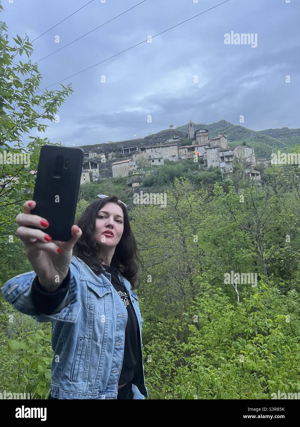 Turista che prende un selfie fronte di un villaggio di montagna abbandonato in Italia Foto Stock