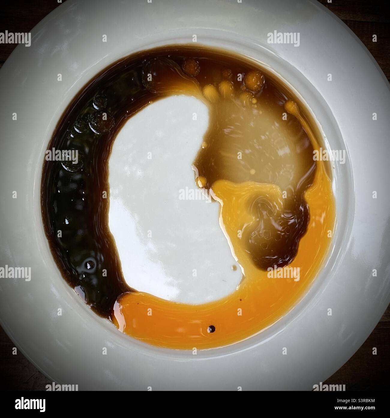 L'olio di peperoncino e l'aceto scuro creano un motivo astratto su un piatto bianco di porcellana - Immagine stock catturata con smartphone