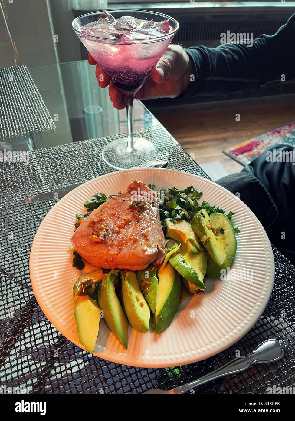 L'uomo gustando un pasto gourmet di tonno scottato con un cocktail cosmopolita in una sala da pranzo residenziale, USA Foto Stock