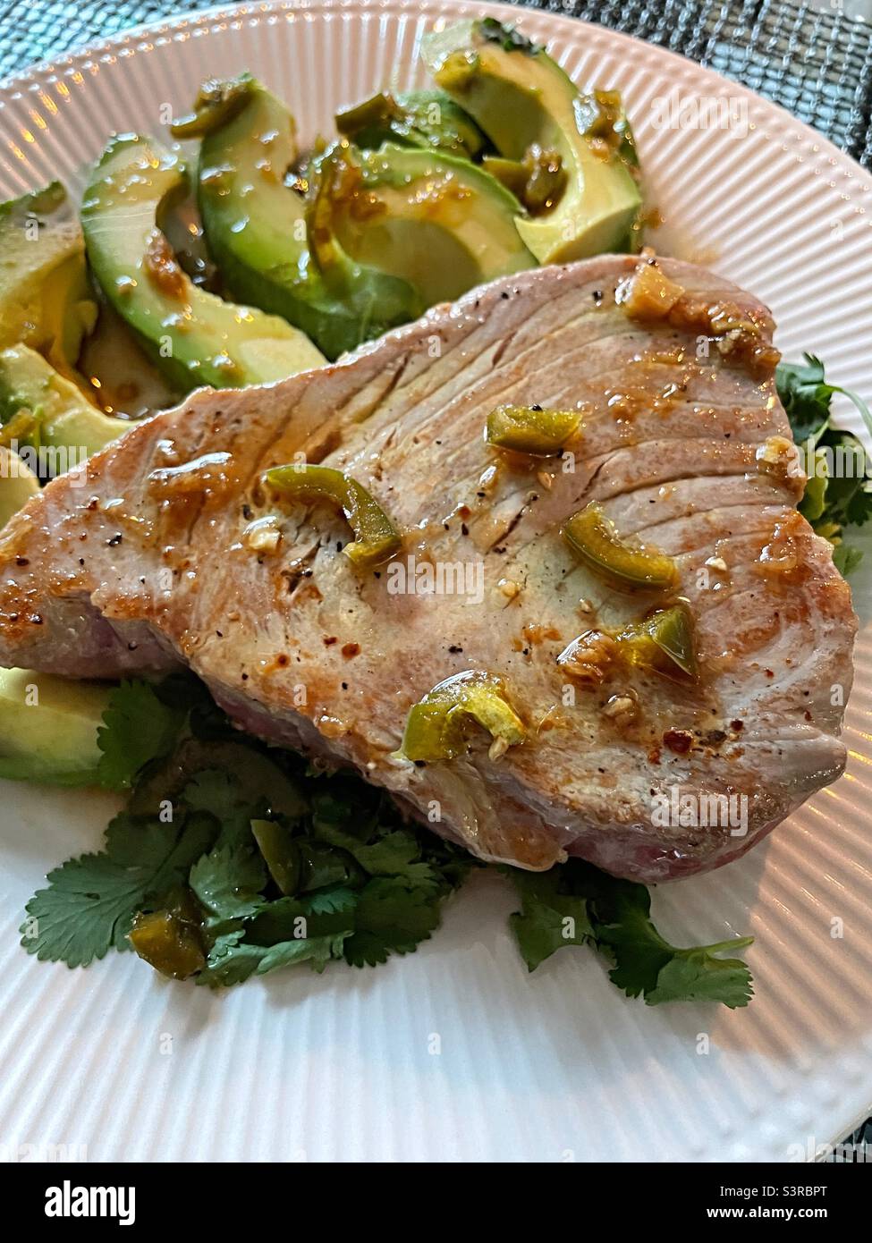 Primo piano di una bistecca di tonno scottata su un letto di coriandolo e avocado a fette con vinaigrette di zenzero di soia lime Foto Stock