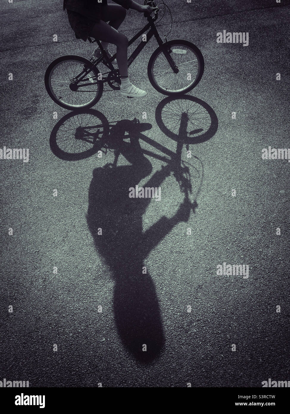 Una ragazza guida la sua bici nel tardo pomeriggio sole e crea un'ombra interessante. Guidare una bicicletta è una cosa eccitante per un bambino da fare - soprattutto al sole! Foto ©️ COLIN HOSKINS. Foto Stock