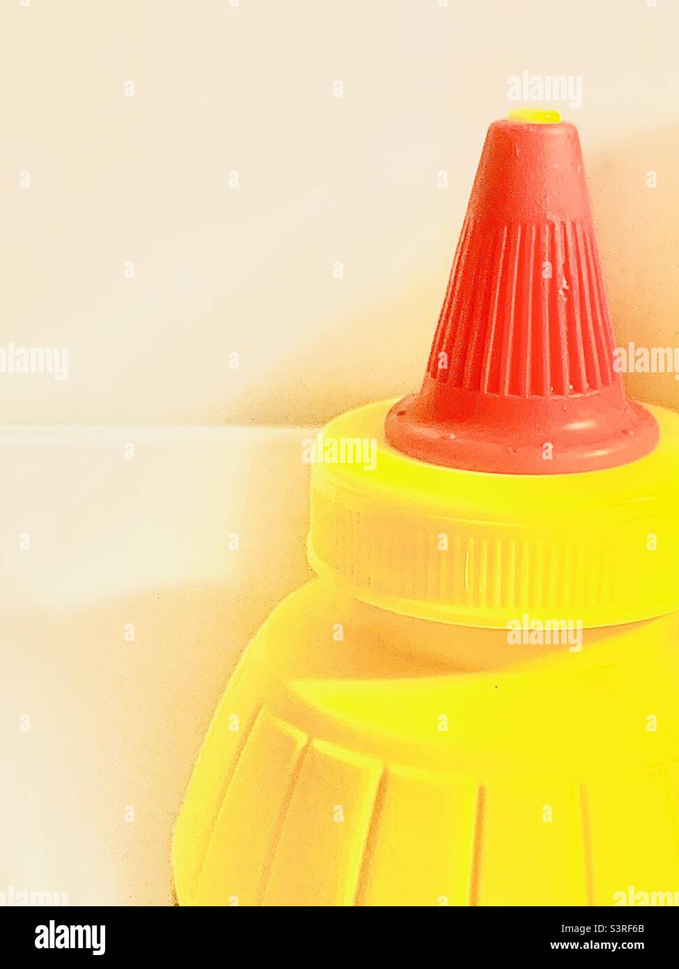 Primo piano di una bottiglia di senape gialla con coperchio rosso sulla destra con sfondo bianco per lo spazio di stampa Foto Stock