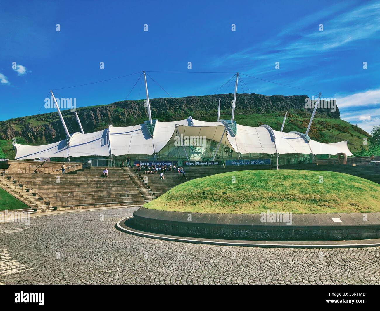 Dynamic Earth, Edimburgo, Scozia in una giornata di sole. Attrazione per famiglie all'avanguardia che porta i visitatori attraverso la storia dal Big Bang ai giorni nostri. Salisbury Crags sullo sfondo. Foto Stock