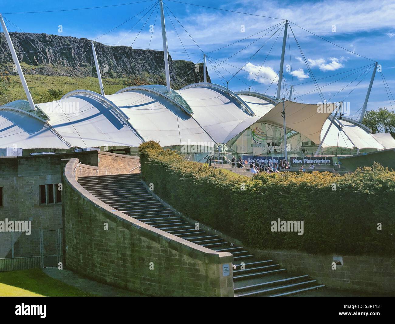 Dynamic Earth, Edimburgo, Scozia in una giornata di sole con cielo blu. Attrazione per famiglie all'avanguardia che porta i visitatori attraverso la storia dal Big Bang ai giorni nostri. Salisbury Crags sullo sfondo. Foto Stock