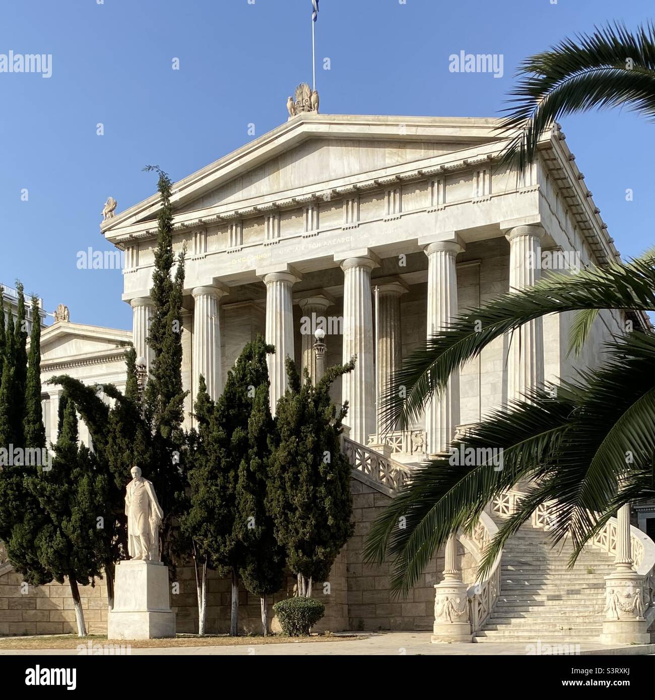 La vecchia Biblioteca Nazionale greca di Atene con una statua (di Bonanos) del suo benefattore Vallianos di fronte. Questo edificio fa parte di una classica trilogia di edifici lungo la via Panepistimiou, Atene. Foto Stock