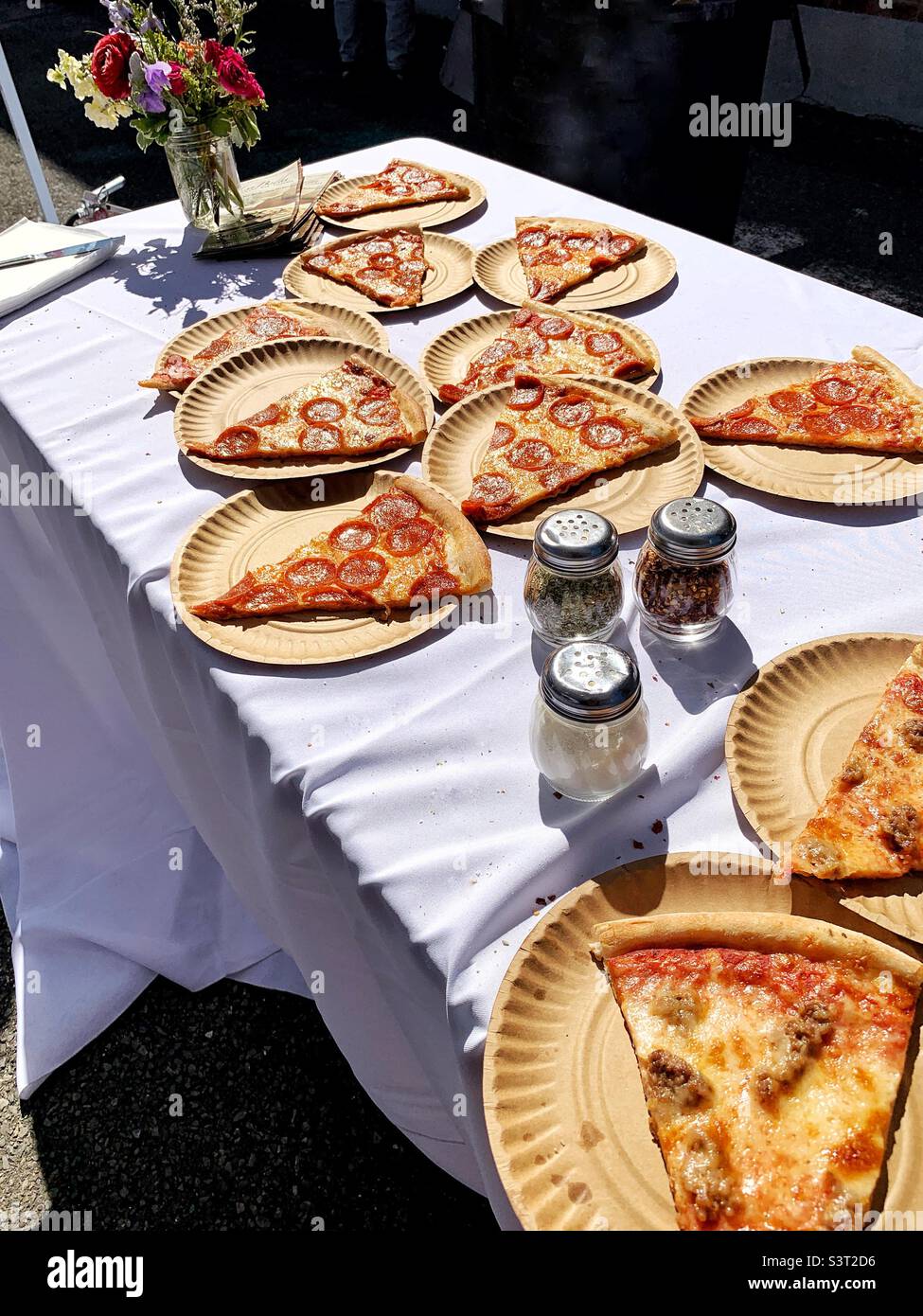Pizza a fette su piatti di carta su un tovagliolo bianco all'esterno Foto Stock