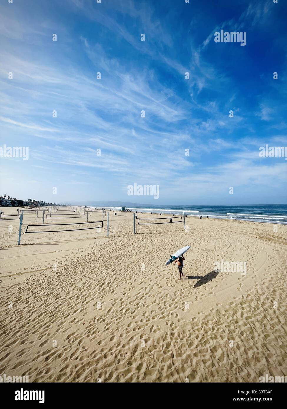 Un maschio pagaia boarder entra dal surf. Manhattan Beach, California stati uniti. Foto Stock