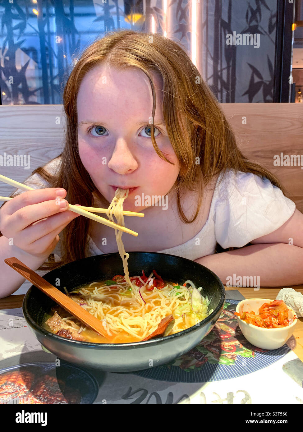 Giovane ragazza che mangia tagliatelle in un ristorante giapponese con bastoncini da tritare Foto Stock
