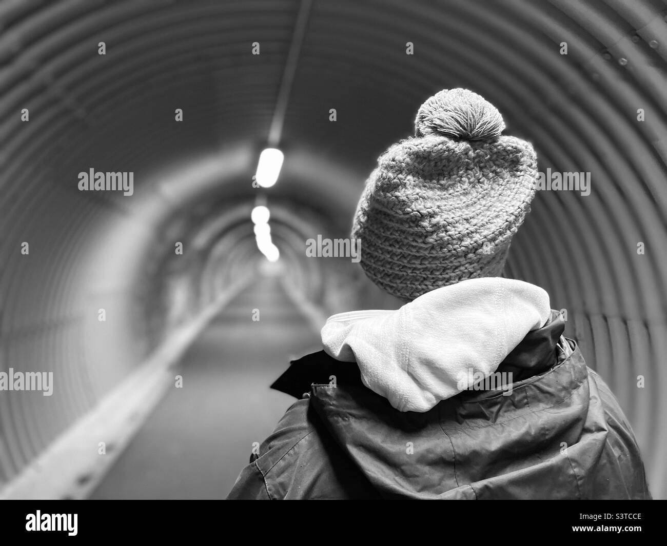 Vista posteriore della donna che indossa un cappello a maglia che cammina in un tunnel Foto Stock
