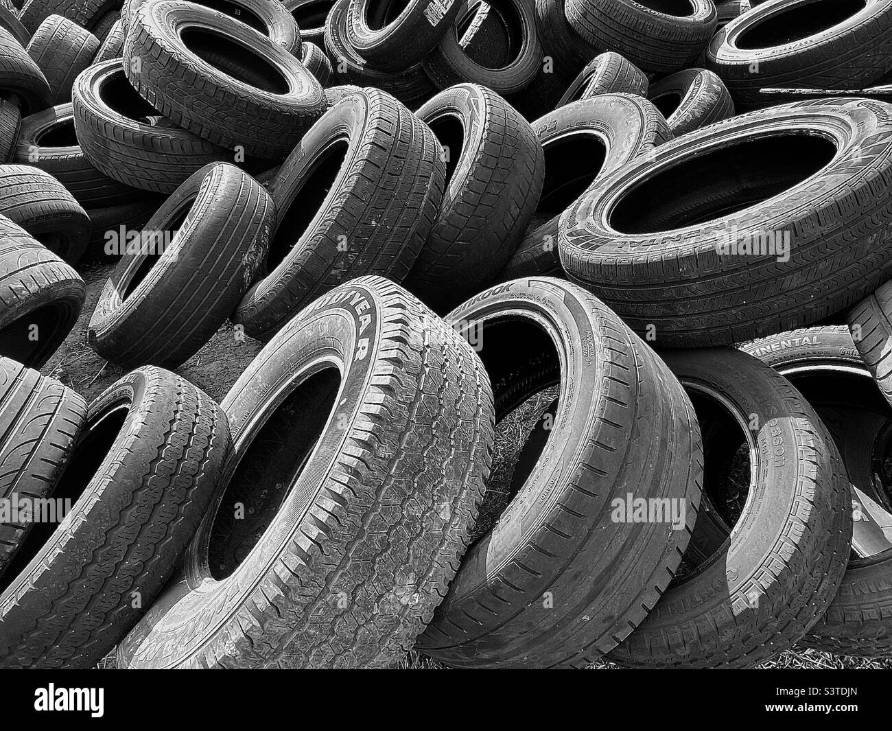 Un mazzo di pneumatici vecchi e usurati si sono accatastati dietro un negozio di auto/pneumatici nello Utah, USA. La desaturazione in bianco e nero e l'aggiunta di un certo contrasto rende un astratto interessante. Foto Stock