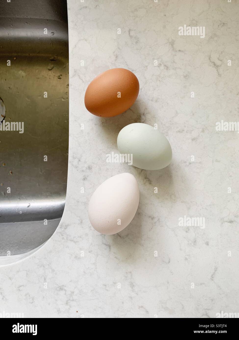 3 uova di diversi colori sul piano di lavoro in marmo bianco in cucina Foto Stock