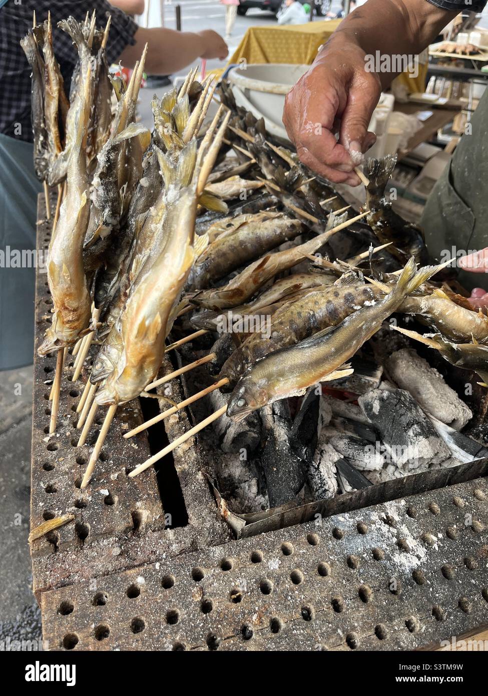 Cibo di strada del festival giapponese - pesce intero alla griglia sui bastoni - Immagine stock catturata con smartphone