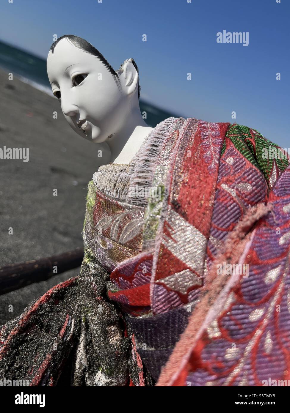 Primo piano di una bambola giapponese rotta che indossa kimono su una spiaggia - Immagine stock catturata con smartphone