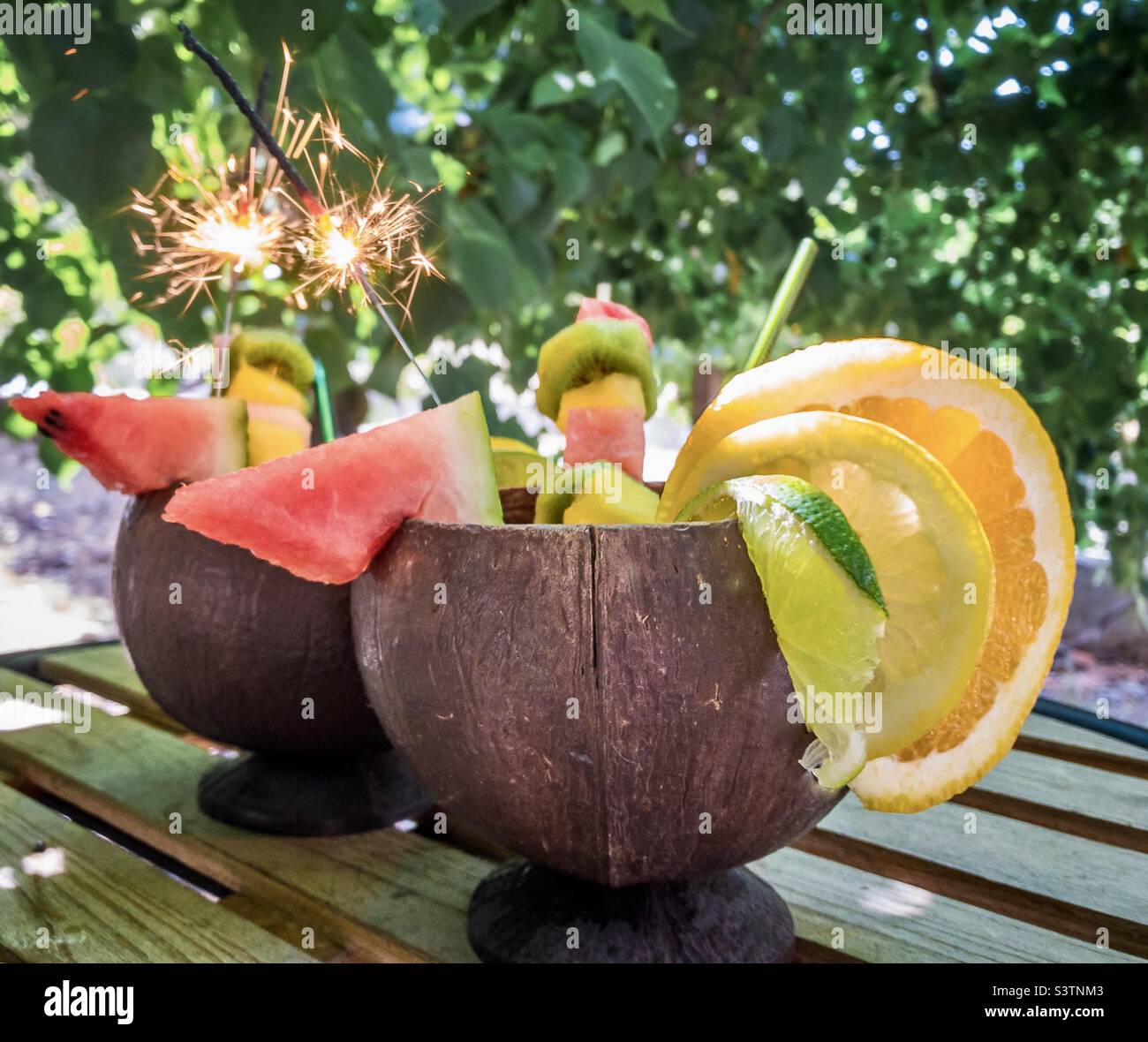 Cocktail fruttati serviti in conchiglie di cocco e con luccicanti all'ombra di un albero - Immagine stock catturata con smartphone