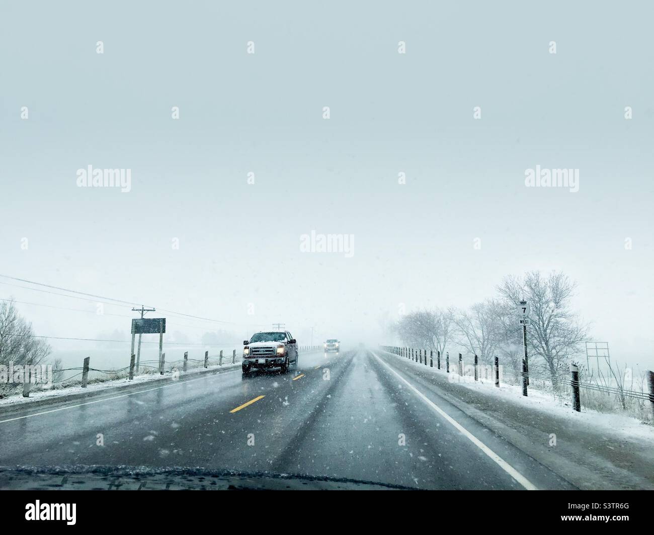 Veicoli che si avvicinano in una tempesta di neve su una strada di campagna, Ontario, Canada. Cielo grande e ominoso. Vista del conducente. Foto Stock