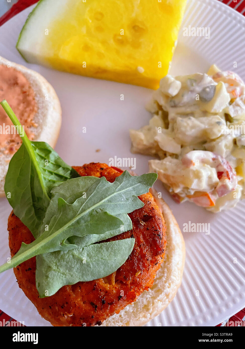Primo piano di un pranzo al sacco festivo di un hamburger di salmone su un hamburger, insalata di patate fatta in casa e una fetta di melone giallo, estate, 2022, Stati Uniti - Immagine stock catturata con smartphone
