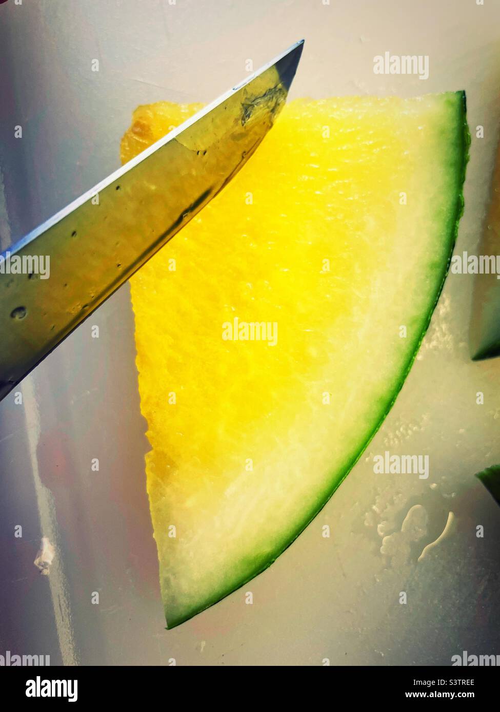 Primo piano di un grande coltello tagliando attraverso una fetta di melone giallo fresco, 2022, USA - Immagine stock catturata con smartphone