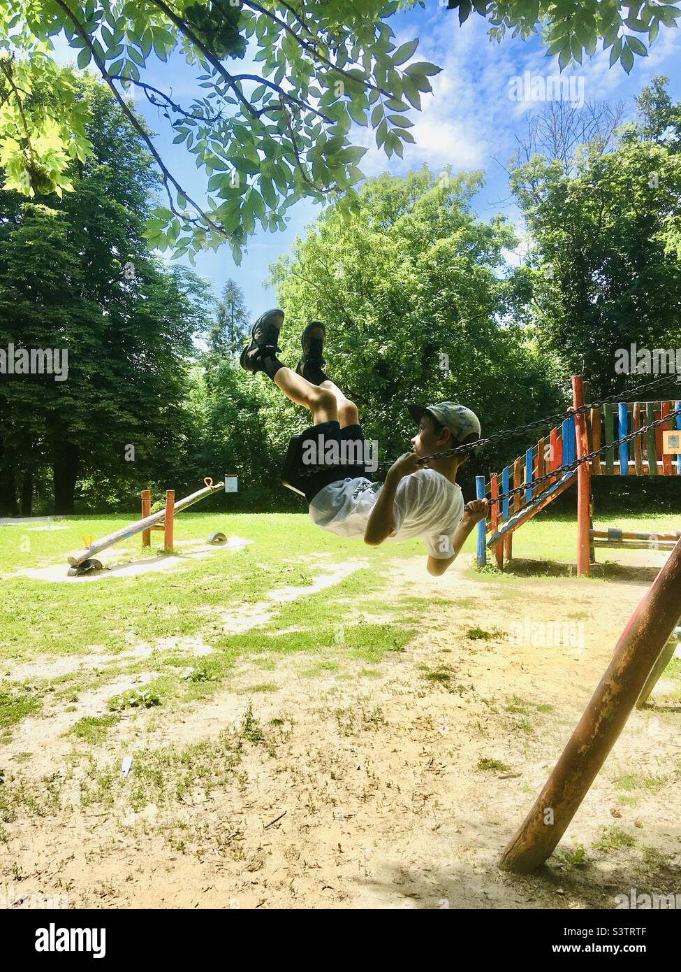 bambino bambino di 8 anni che oscilla al parco giochi così alto che quasi raggiungere rami di albero Foto Stock