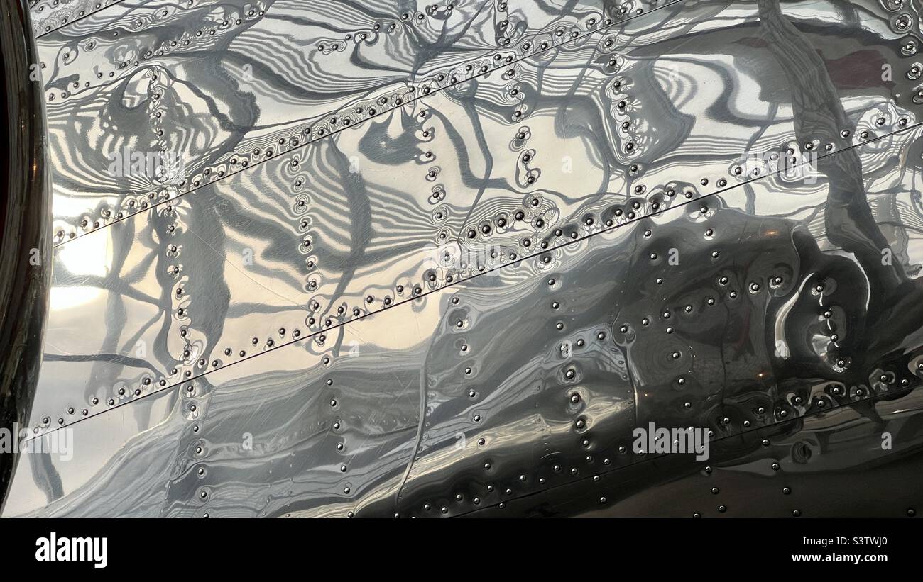 Particolare di velivolo rivestito in pannelli metallici lucidati, rivettati in posizione con riflessi astratti. Adatto per lo sfondo per grafica e testo - Immagine stock catturata con smartphone