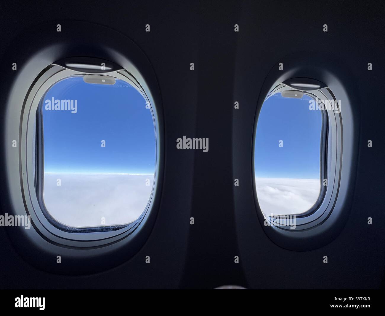Guardando attraverso le finestre di aeroplano con le nuvole bianche e morbide sotto e profondo cielo indaco sopra Foto Stock