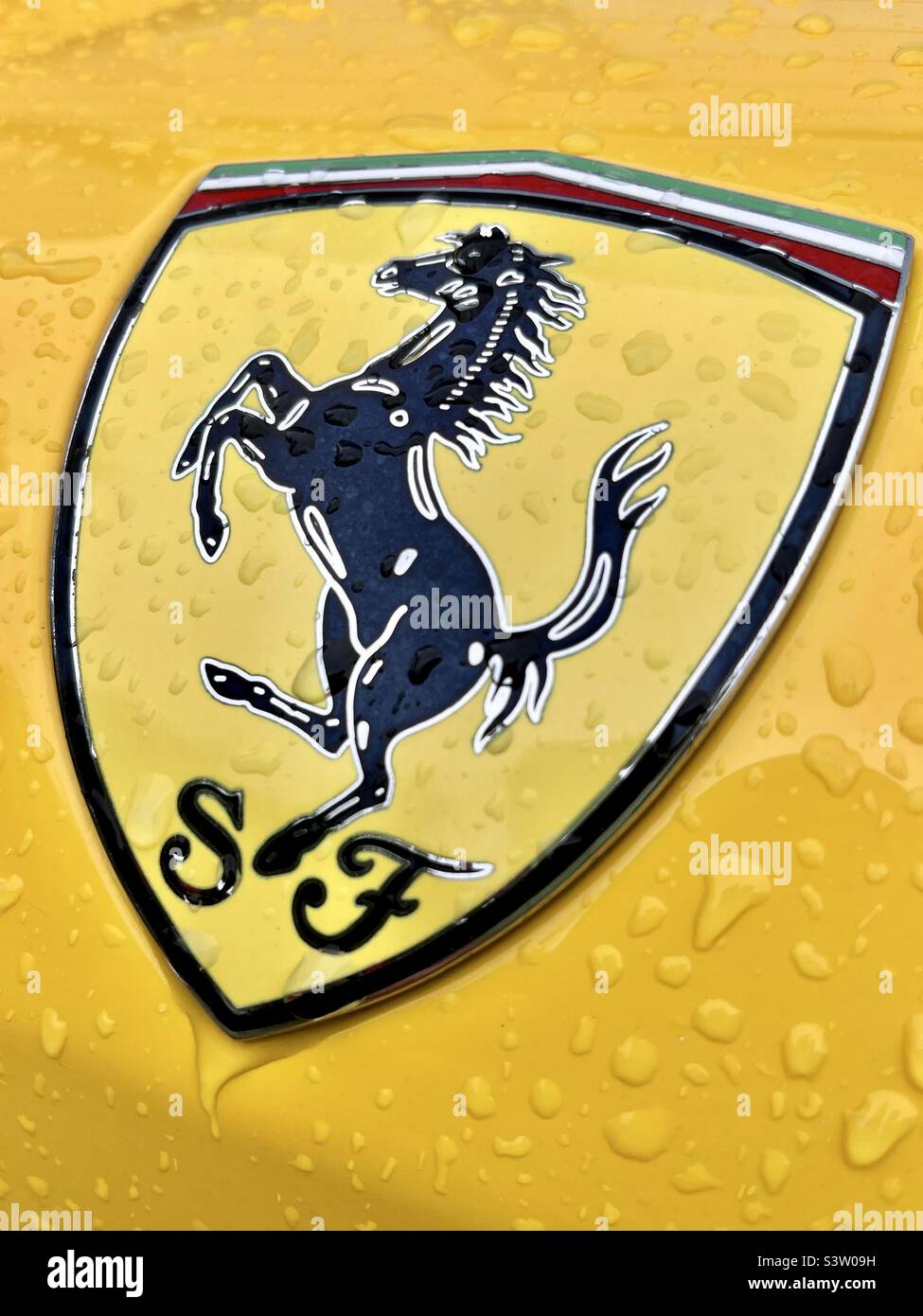 Logo Ferrari Horse e cartello primo piano su un'auto bagnata gialla con gocce di pioggia - Immagine stock catturata con smartphone