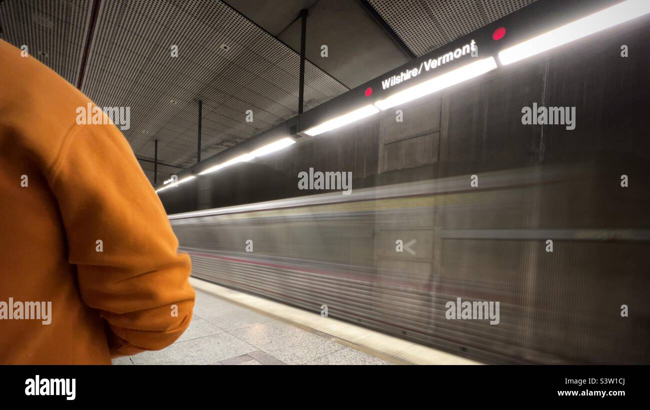 LOS ANGELES, CA, GENNAIO 2022: Bordo della persona che indossa una felpa arancione in piedi sulla piattaforma mentre il treno Blurred Line arriva alla stazione di Wilshire-Vermont sulla metropolitana LA Metro Foto Stock
