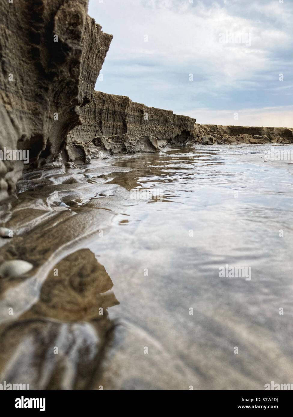Primo piano della scarpa di un piccolo fiume che attraversa una spiaggia e che scorre nel Mar Baltico dando l'impressione di essere una grande scogliera, a soli 20 cm di altezza in realtà - Immagine stock catturata con smartphone