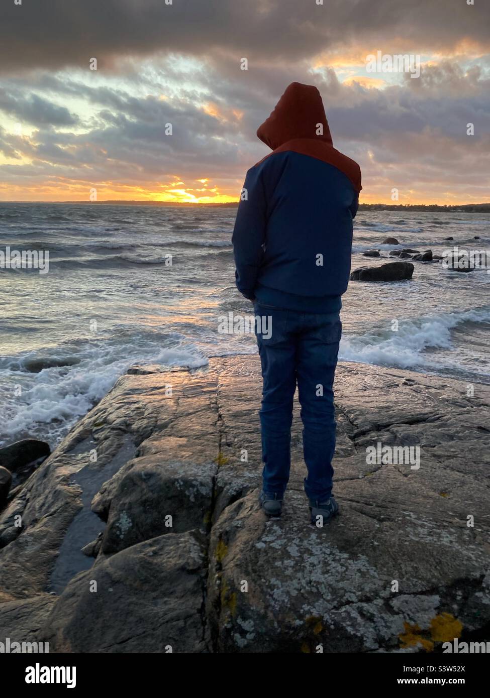 Un ragazzo pre-teenager che si erige nel Mar Baltico sulla costa occidentale della Svezia durante una tempesta Foto Stock