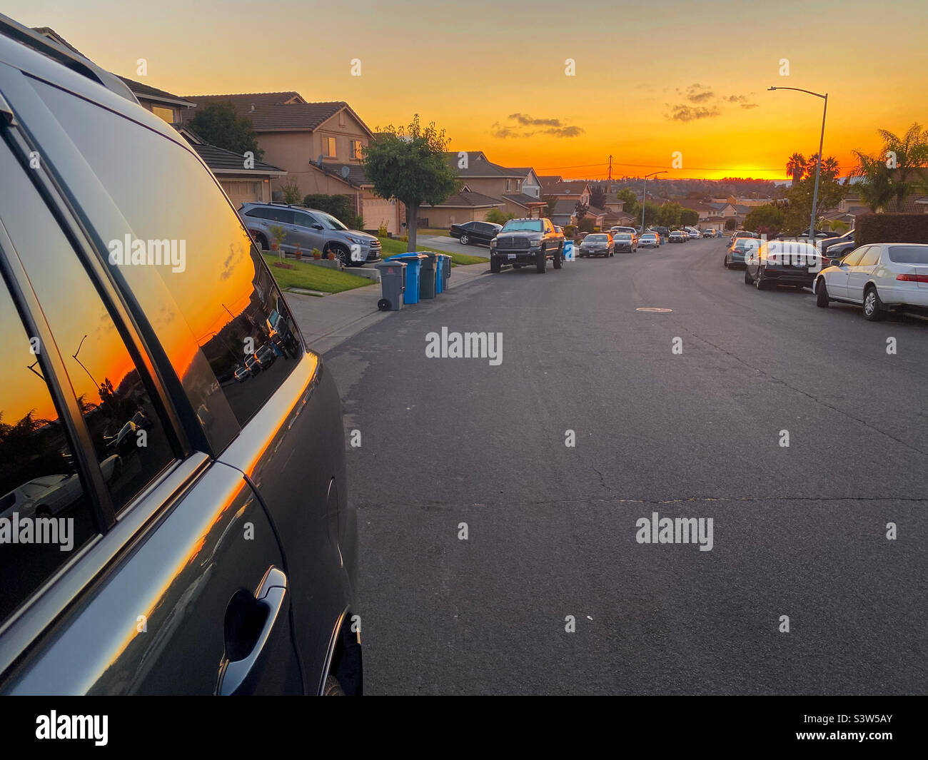 Cielo arancione alla fine di una strada suburbana a Vallejo, California, con un bagliore arancione nel cielo che si riflette sul lato di un'auto. Foto Stock