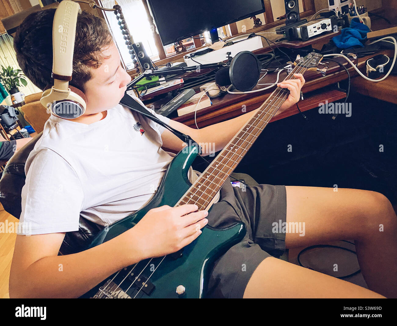 Un ragazzo che pratica a suonare la chitarra base indossando le cuffie. Foto Stock