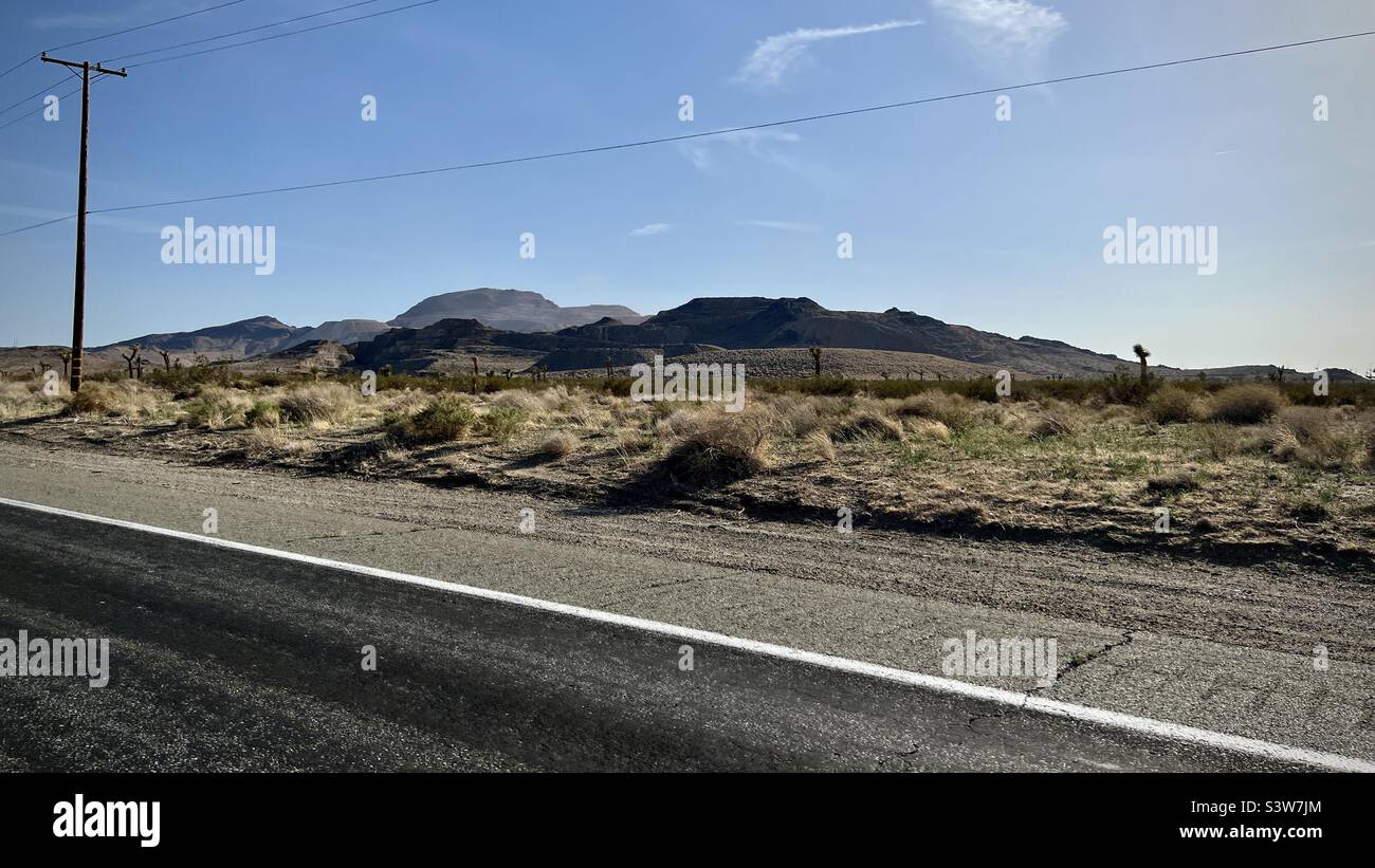 Vista dall'autostrada attraverso il deserto di Mojave in California, con macchia e montagne in lontananza, telegrafo pali e fili accanto alla strada Foto Stock