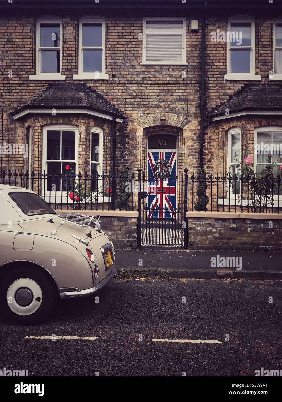 Strada britannica in vecchio stile con bandiera Union Jack dipinta sulle porte e auto d'epoca o retrò Foto Stock