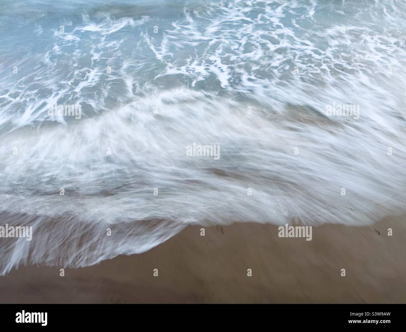 Esposizione lunga - piccole onde che si rompono su una spiaggia Foto Stock