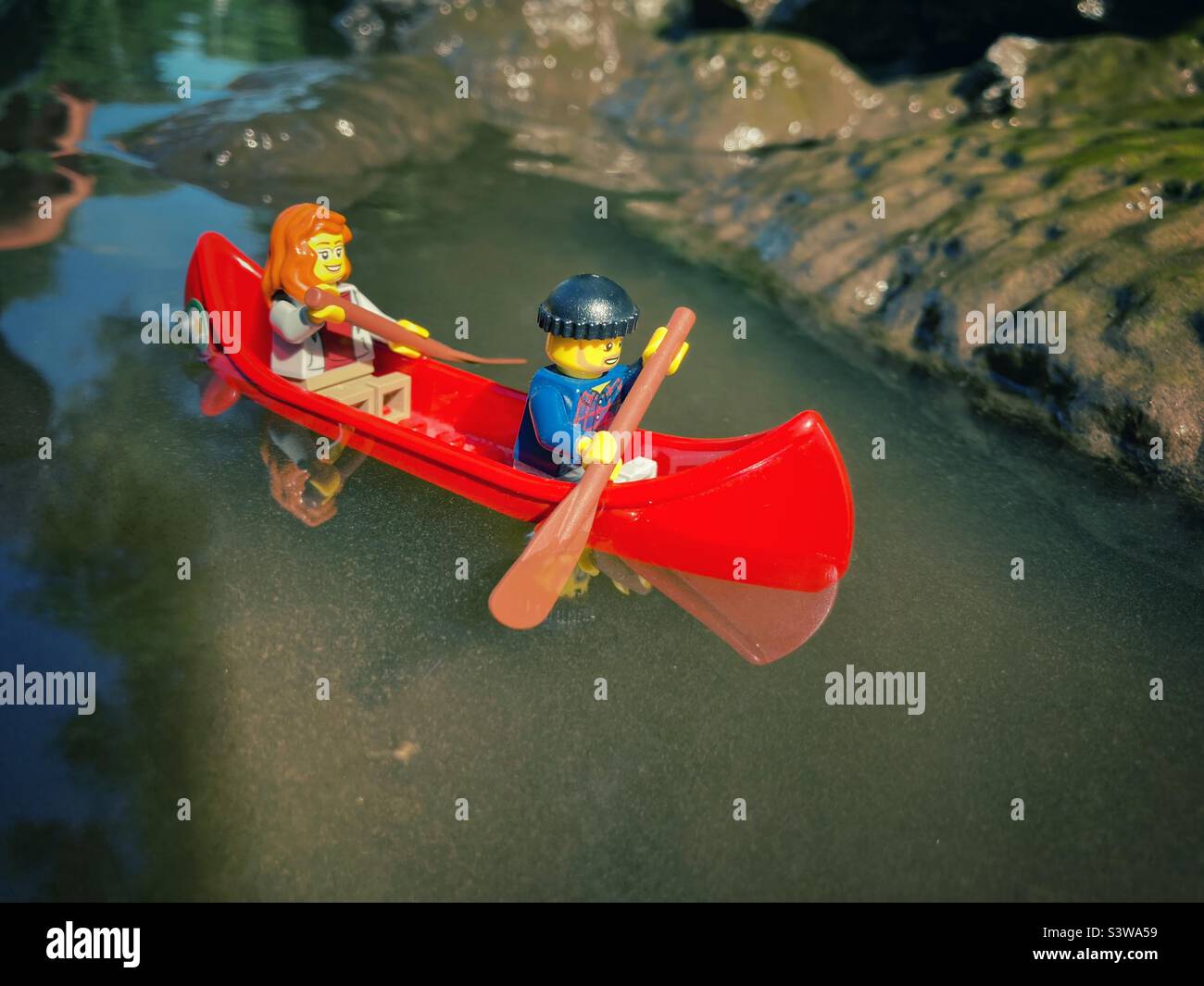 Due figure Lego in canoa rossa su acqua fangosa - Immagine stock catturata con smartphone