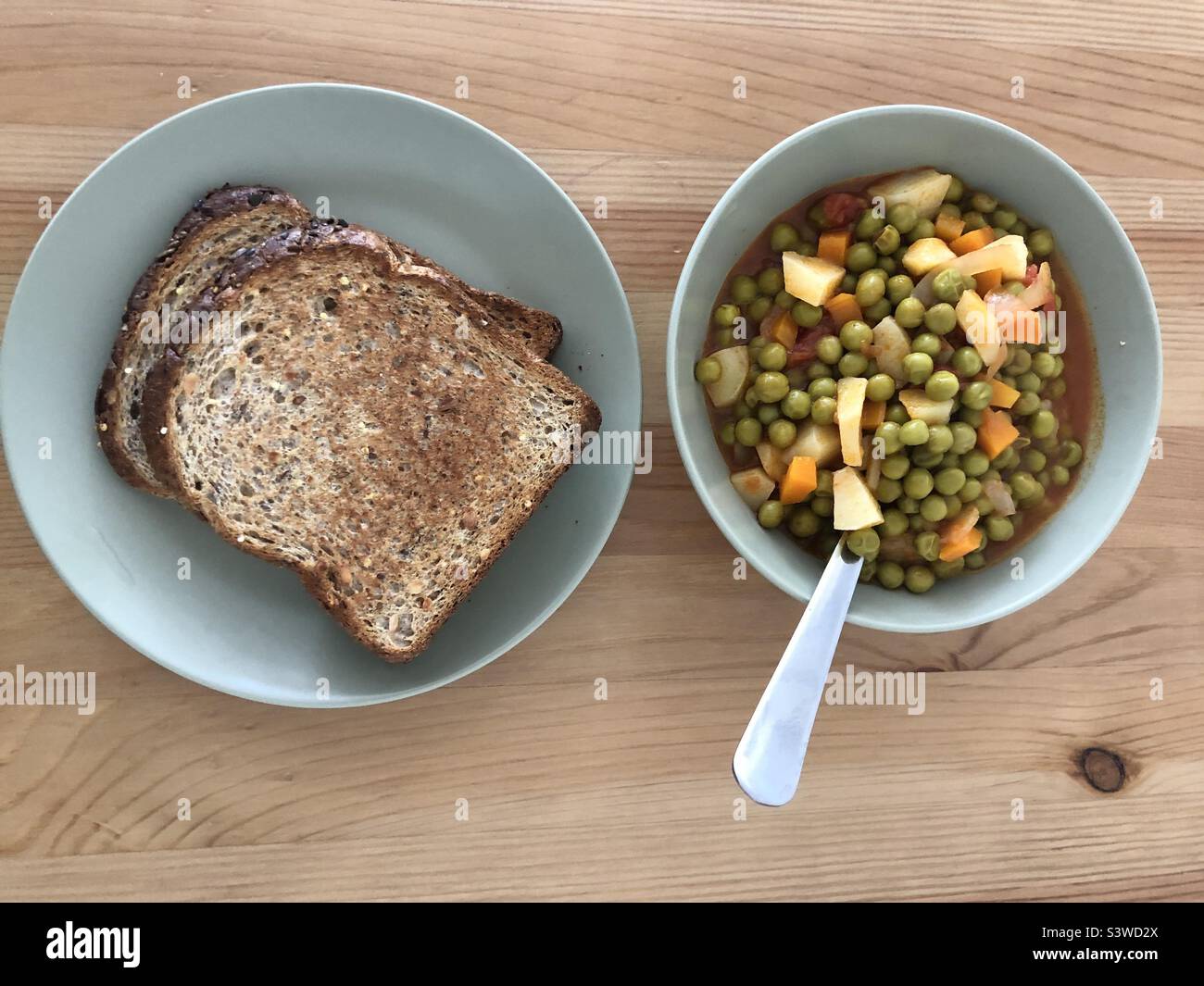 Piatto vegano, patate e verdure con piselli verdi in umido servite con pane affettato - Immagine stock catturata con smartphone