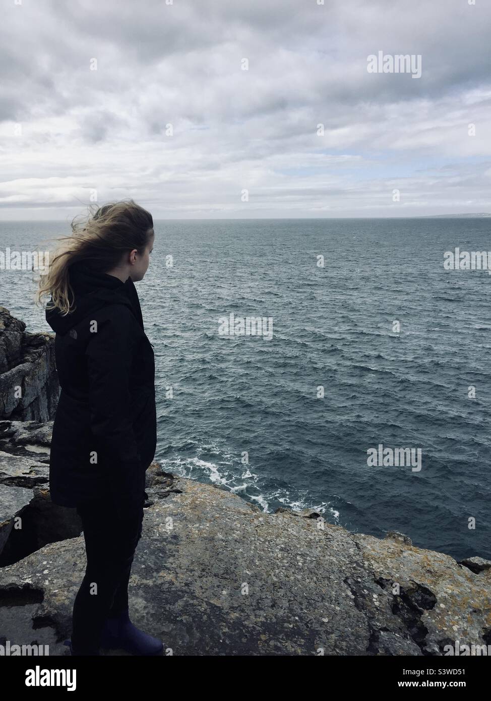 Giovane donna che si affaccia sul mare mentre esplora il Burren a Oughtdarra, Co. Clare, Irlanda. - Immagine stock catturata con smartphone