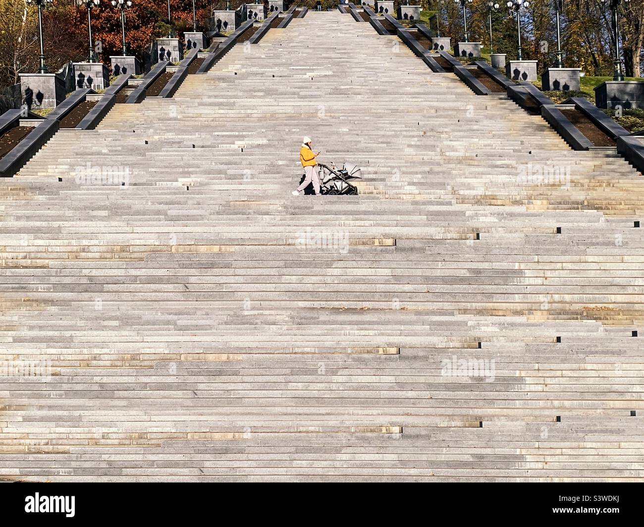 Giovane donna in mantello giallo che cammina per scale nel parco Foto Stock