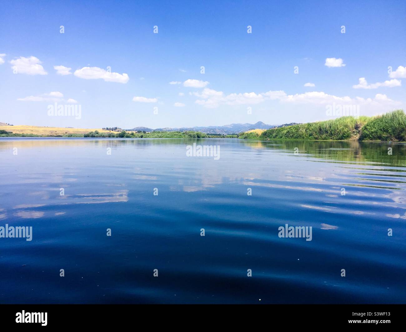 Galleggiando lungo un fiume in uno splendido pomeriggio estivo. Cielo blu, acqua blu fredda e alcune nuvole in lontananza. Foto Stock