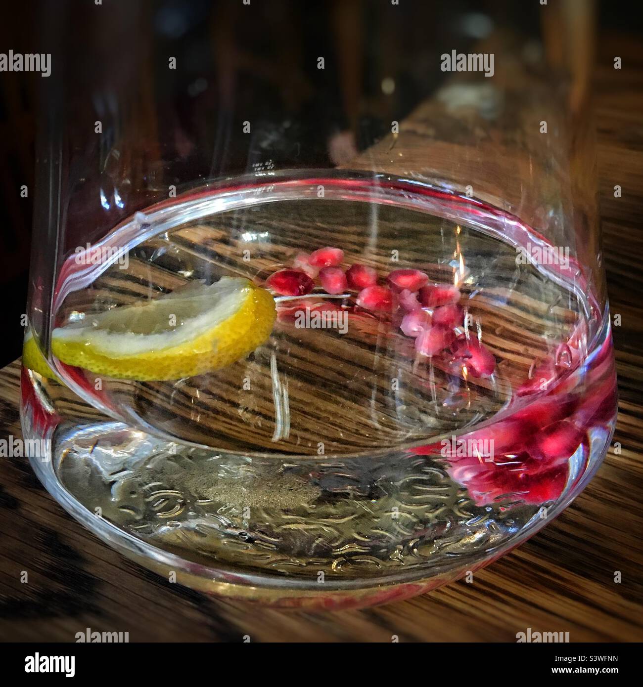 Semi di melograno e una fetta di limone in un bicchiere d'acqua Foto Stock
