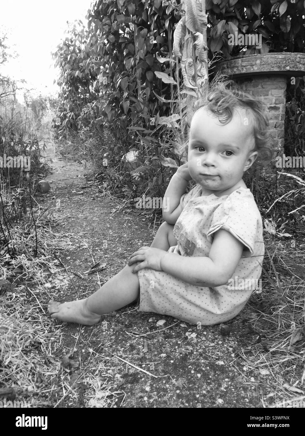 Bambino seduto nel giardino mono Foto Stock