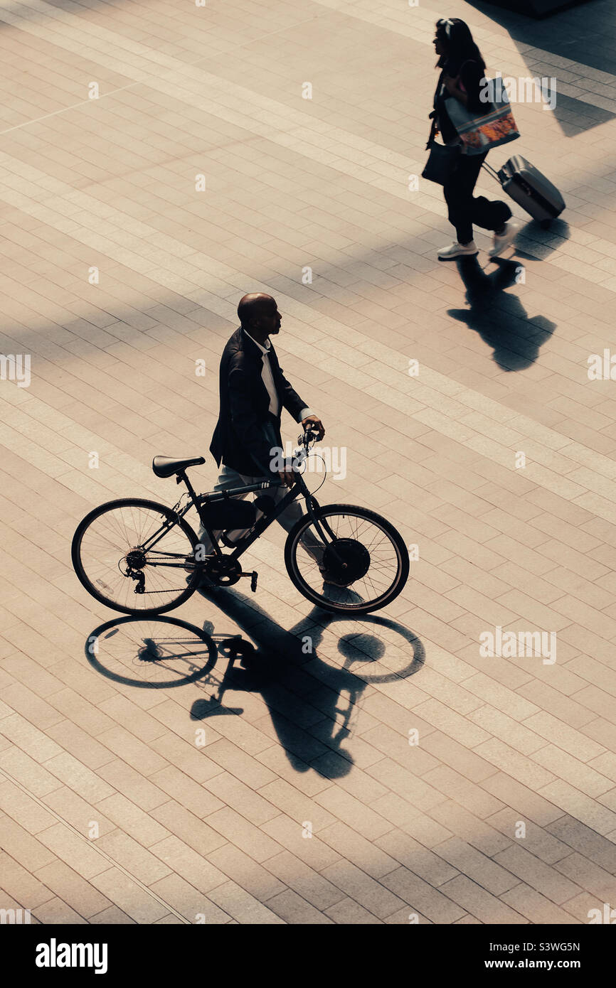 Vista ad angolo alto dell'uomo e della donna che spingono una bicicletta con ombre in ambiente urbano - Immagine stock catturata con smartphone